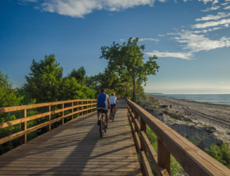 Małżeństwo na rowerach na drewnianym moście obok plaży.